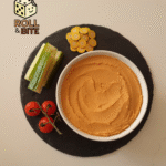 Sundried tomato hummus in a bowl with a side of cucumbers and cherry tomatoes.